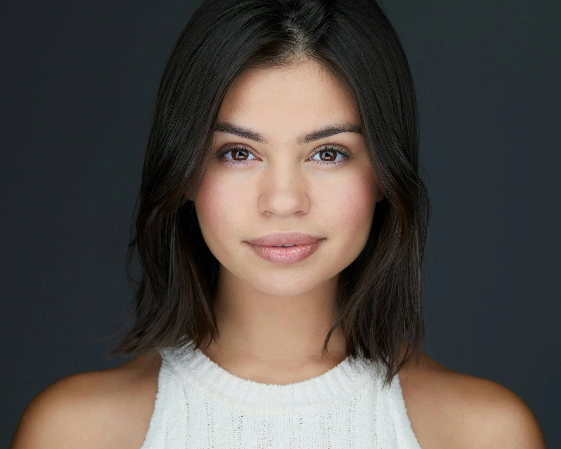 Actor headshot of a young woman with shoulder-length dark hair against a charcoal backdrop